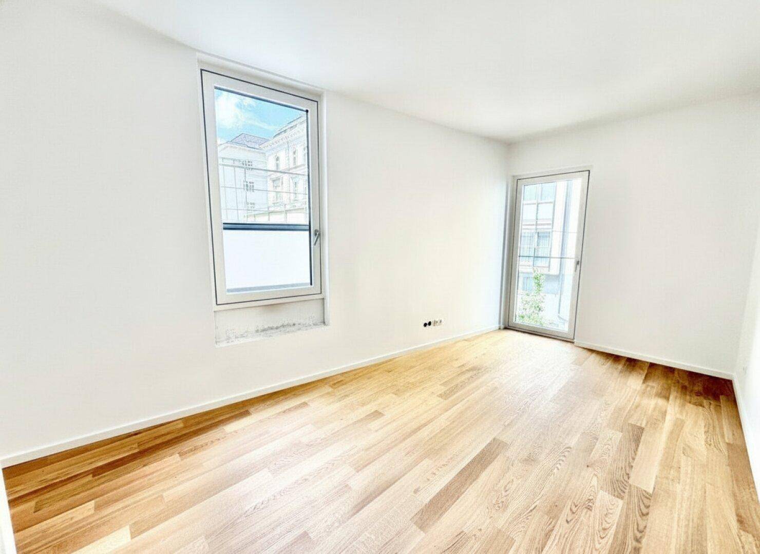 Leeres Schlafzimmer mit hellem Holzparkett, großem Fenster und Zugang zu einem Außenbereich.