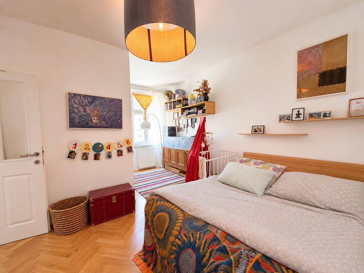Gemütliches Schlafzimmer mit Holzbett, farbenfroher Dekoration und einem Bereich für ein Babybett.