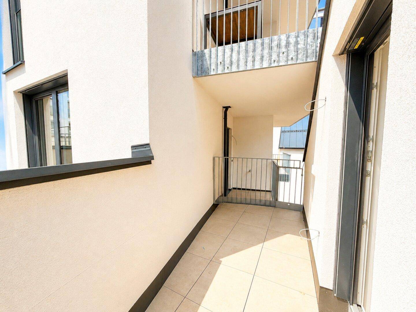 Schmaler Balkon mit Fliesenboden und Metallgeländer, bietet Platz im Freien.