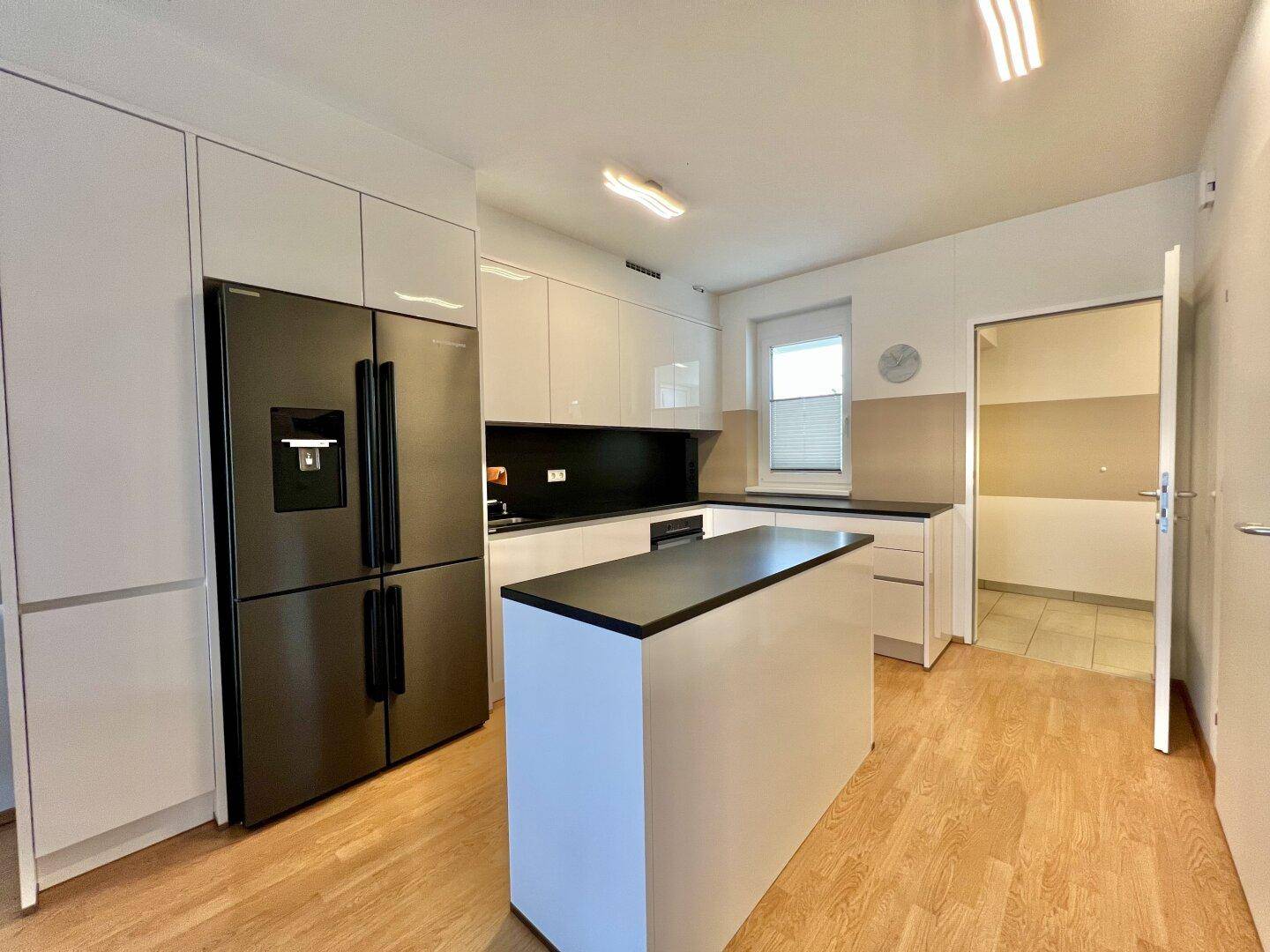 Moderne Einbauküche mit weißen Hochglanzfronten, Kochinsel und großem Kühlschrank.