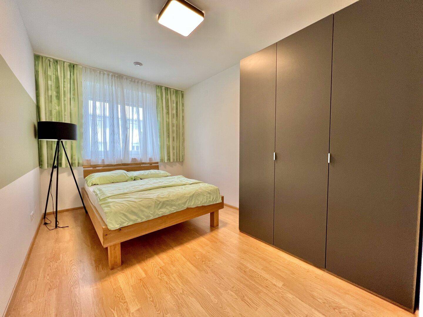 Schlafzimmer mit hellem Holzbett, großem Kleiderschrank und Laminatboden.