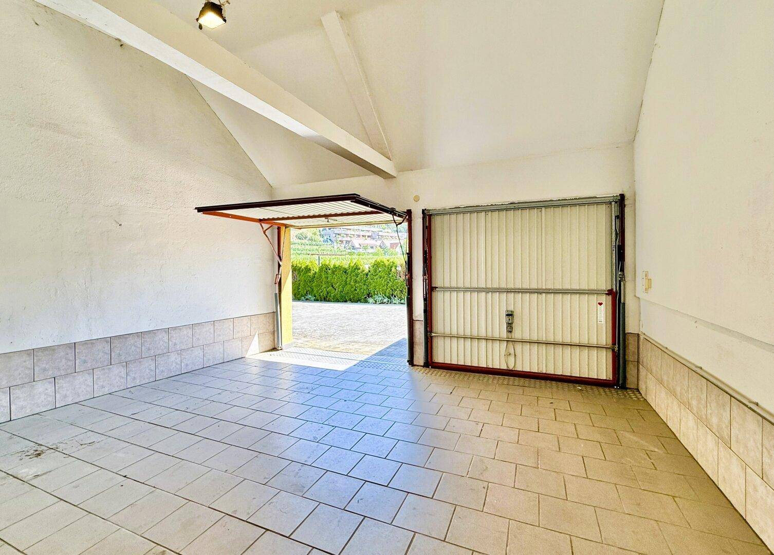 Geräumige Garage mit Fliesenboden und zwei Rolltoren, bietet Platz für Fahrzeuge.