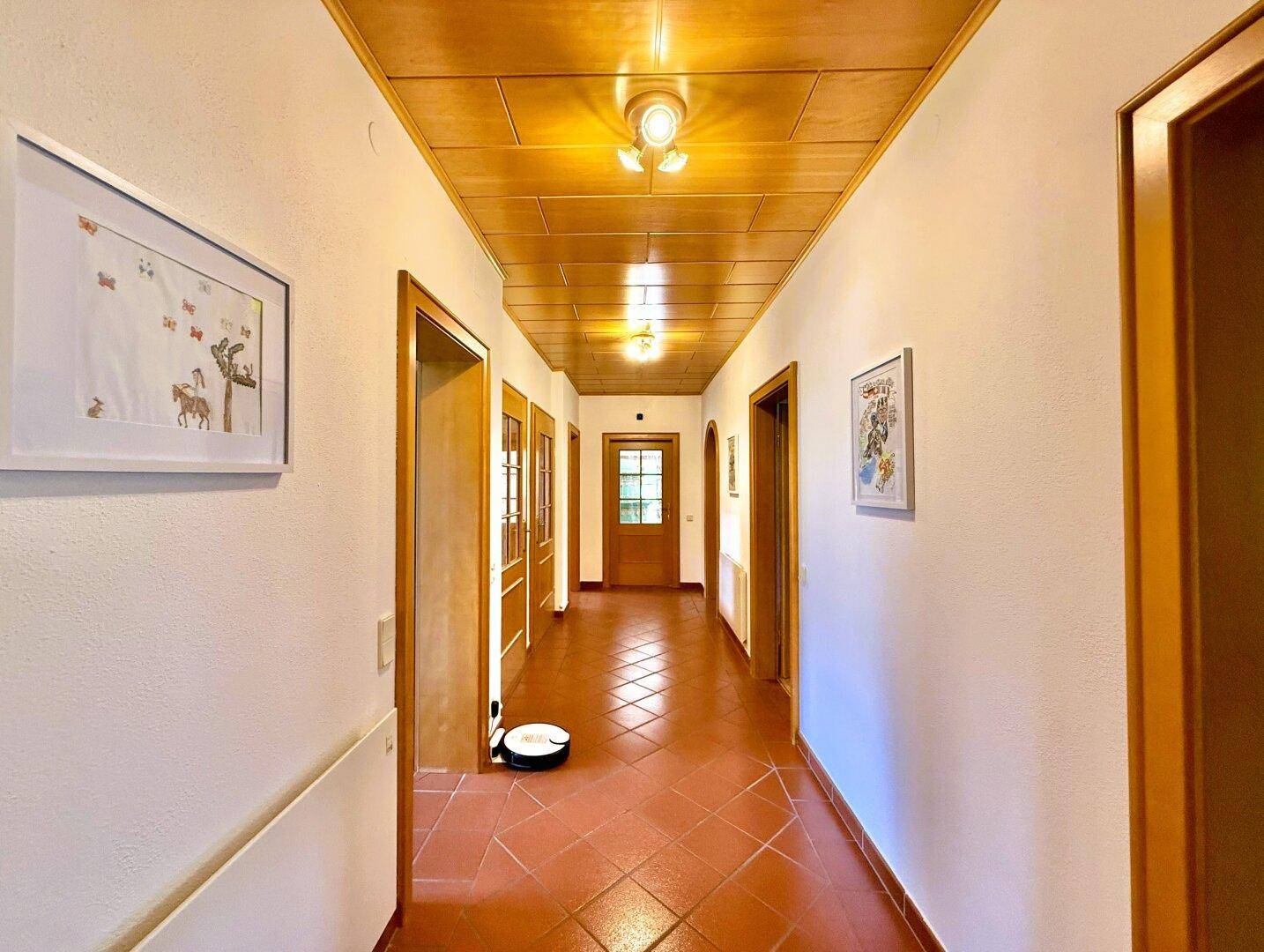Langer Flur mit Terrakottafliesen und Holzdecke, der verschiedene Räume verbindet.