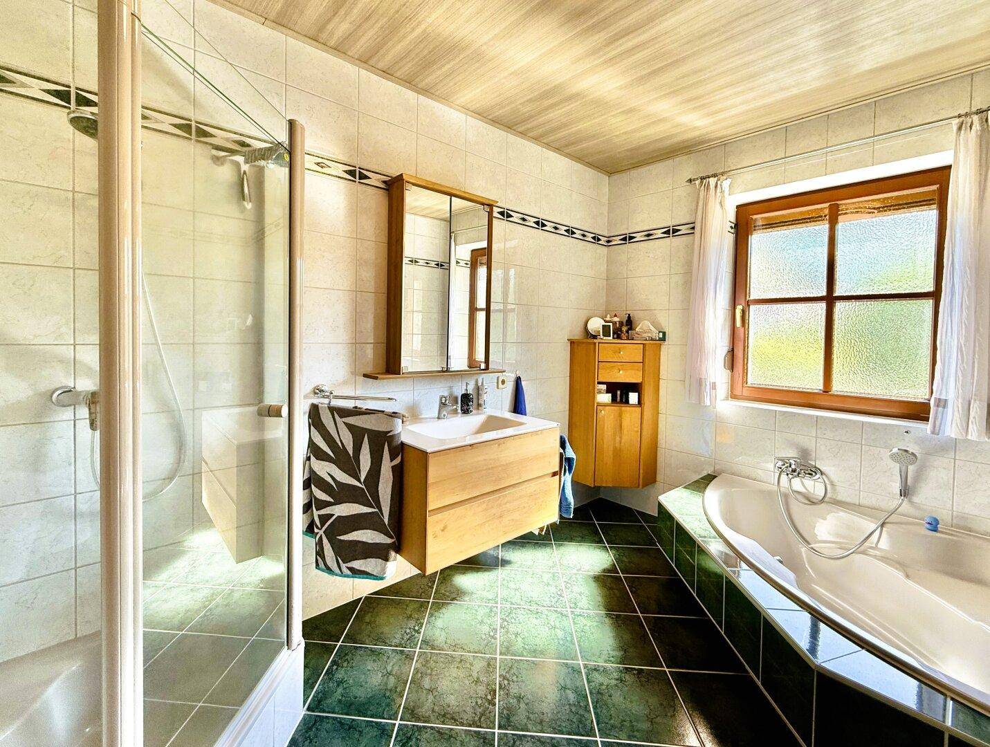 Geräumiges Badezimmer mit Badewanne, Dusche und Fenster, gefliest in Grün- und Weißtönen.
