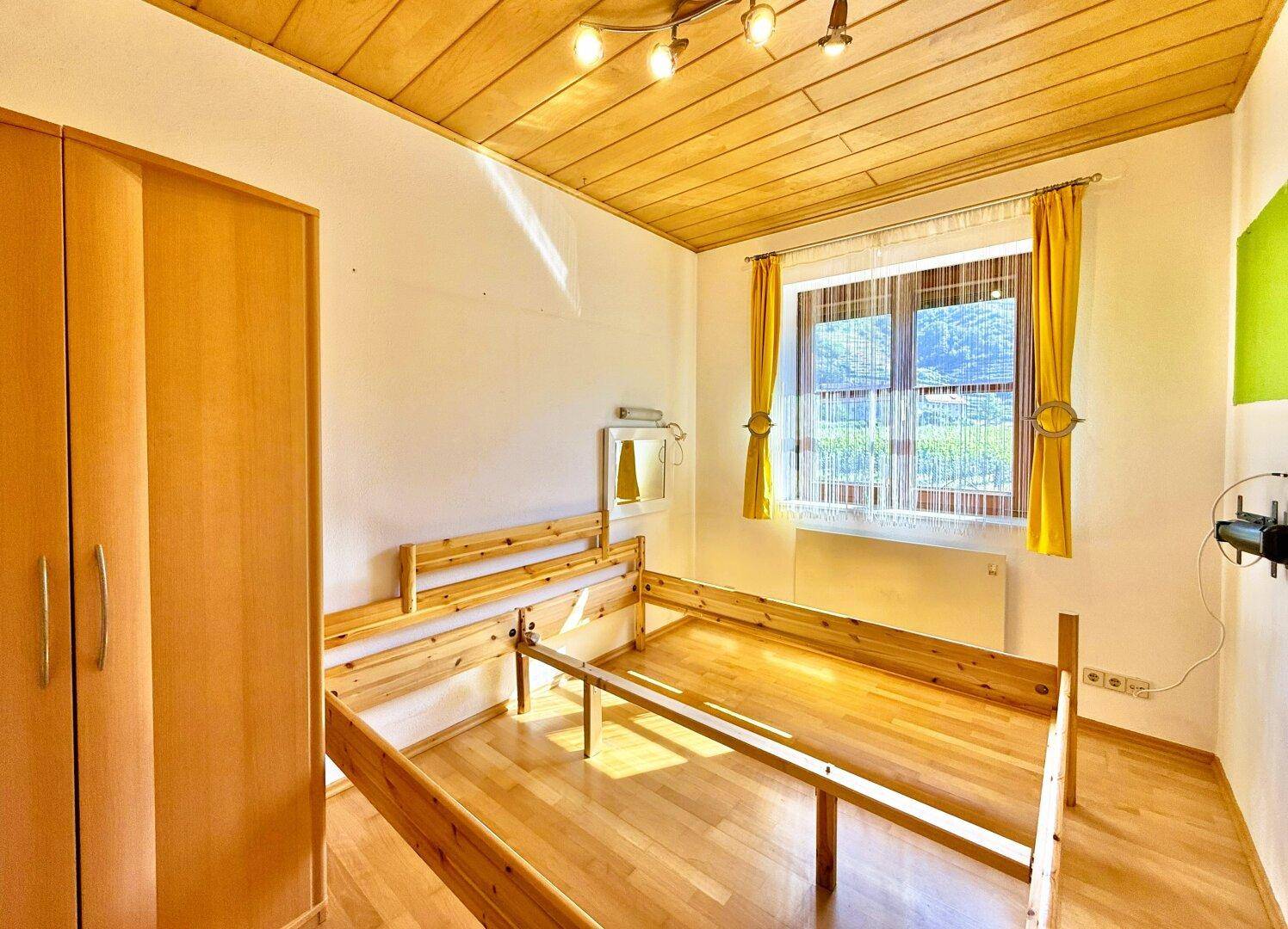 Schlafzimmer mit Holzboden und Holzdecke, ausgestattet mit einem Bettrahmen und Kleiderschrank.