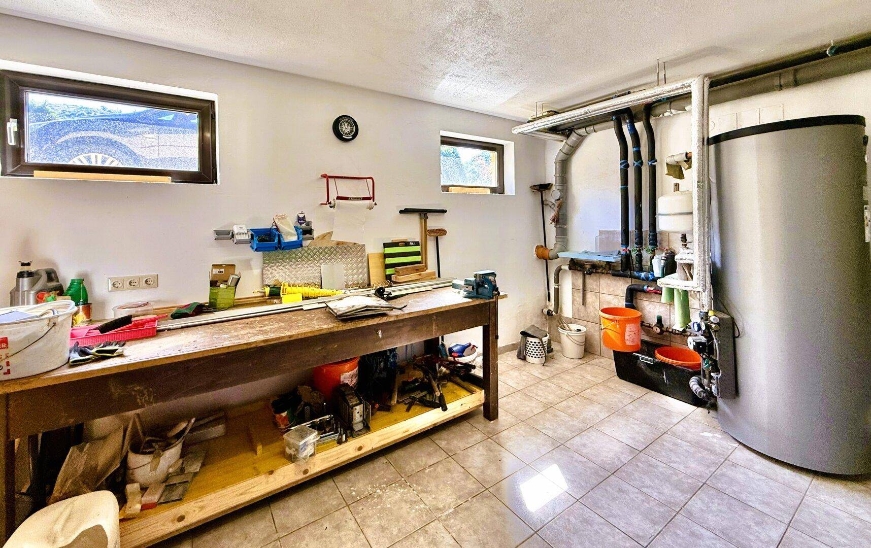 Werkstatt im Keller mit Arbeitsbank, Heizungsanlage und Fliesenboden.