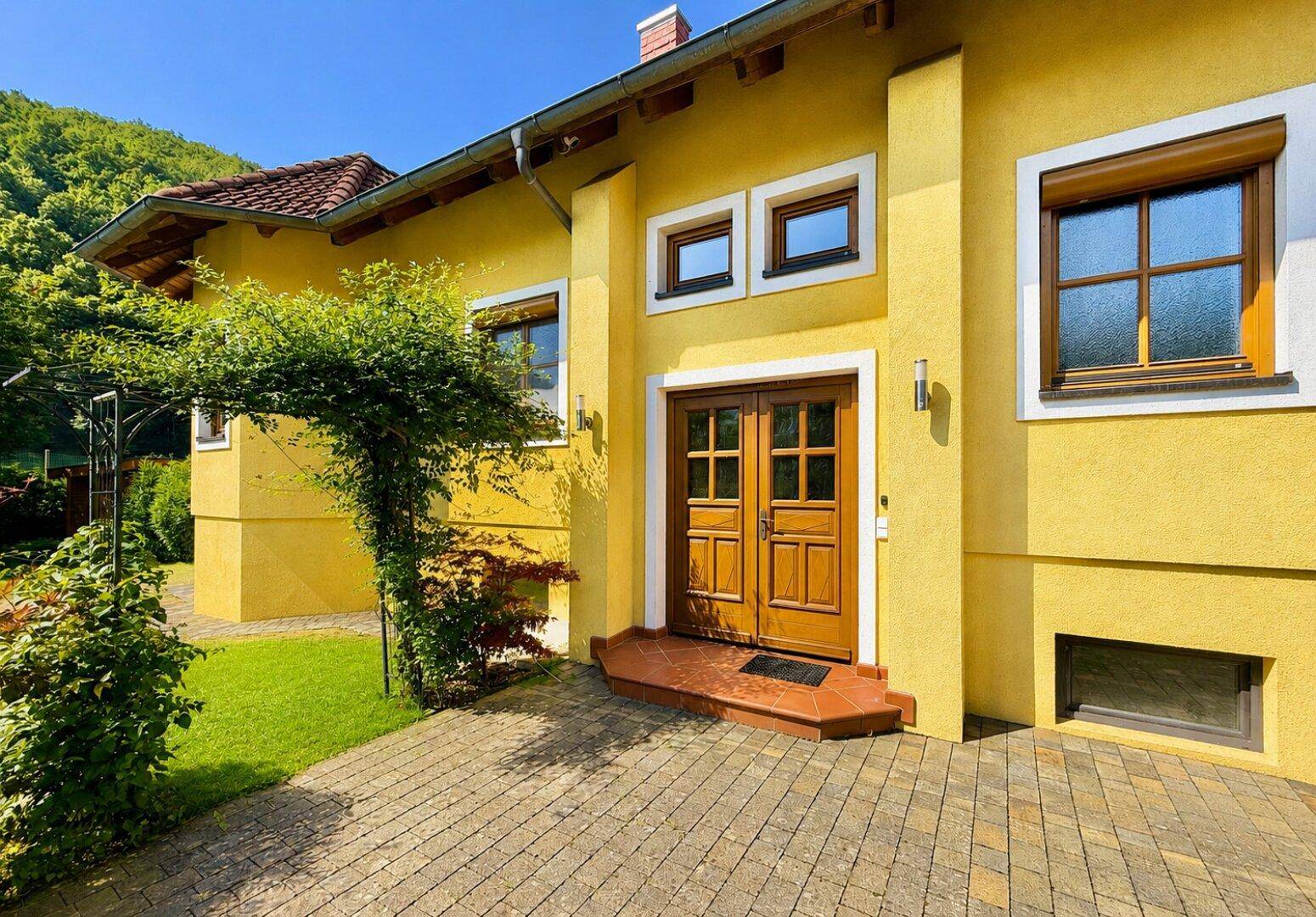Hauptfassade des gelben Hauses mit Holztür und gepflastertem Eingangsbereich.
