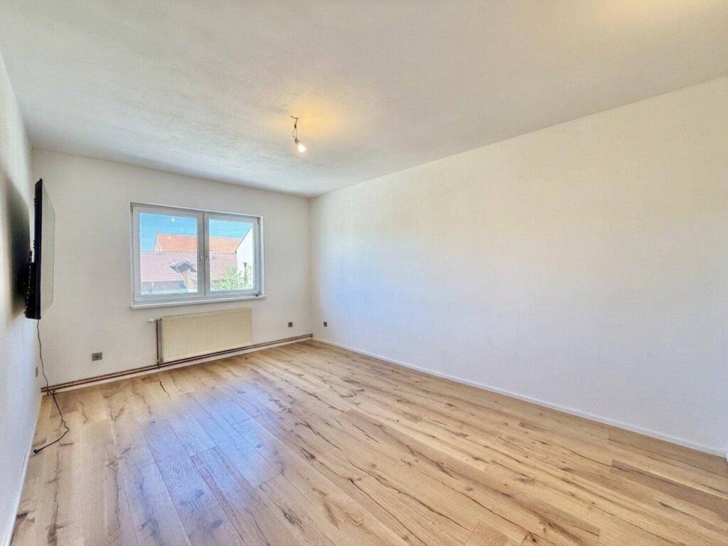 Heller Raum mit Laminatboden, weißen Wänden und Blick auf die Umgebung durch das Fenster.