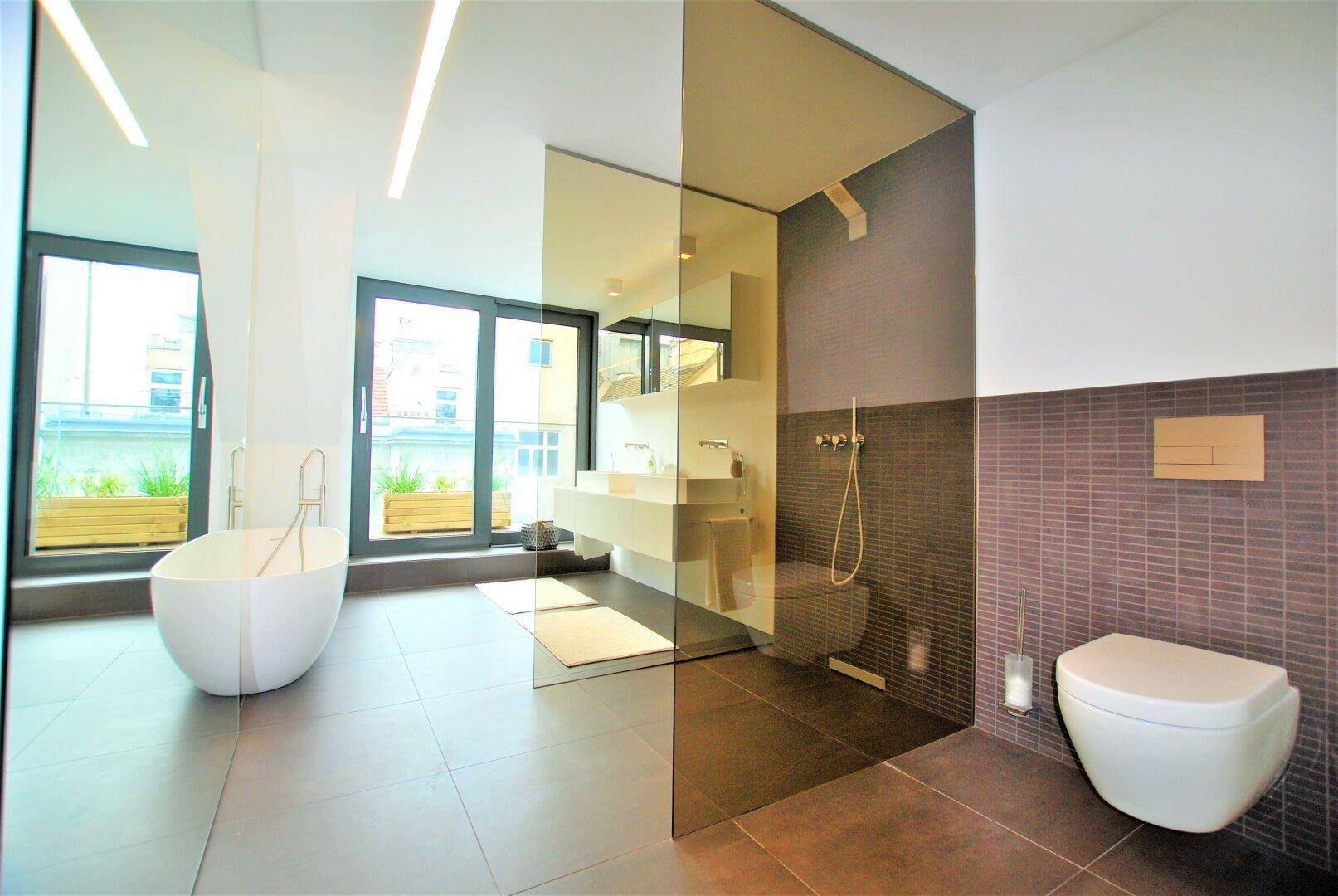 Luxuriöses Badezimmer mit freistehender Badewanne, Doppelwaschbecken und großer Glasdusche, hell durch große Fenster.