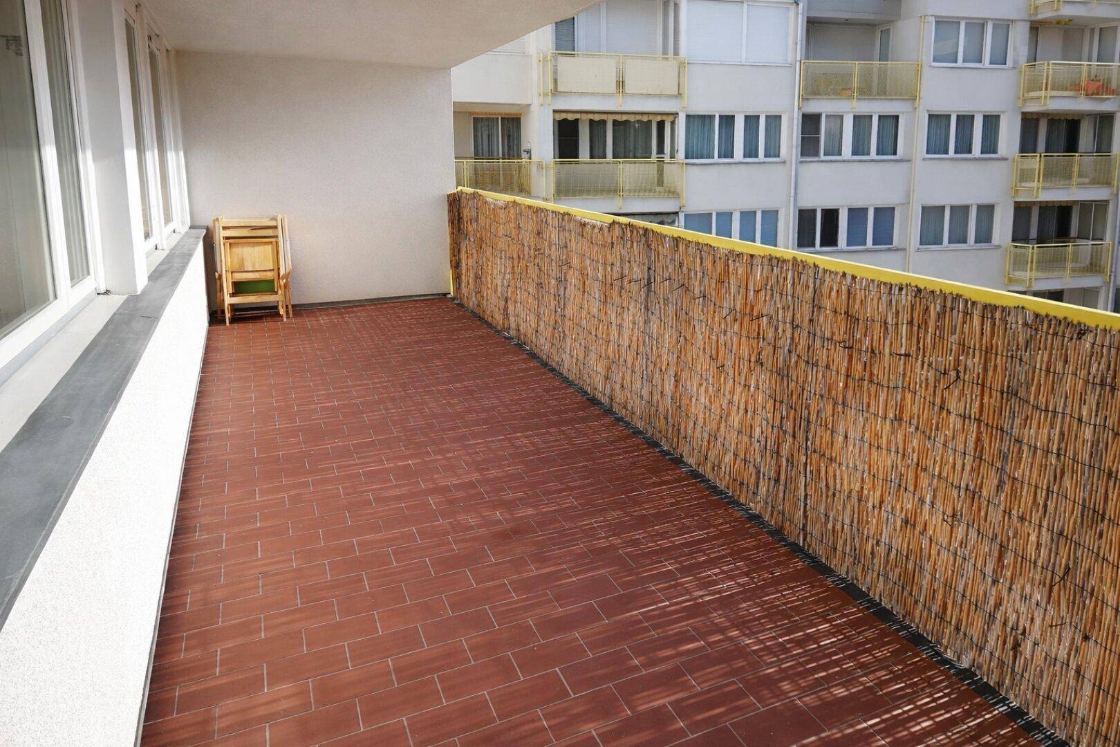 Geräumiger Balkon mit Terrakottafliesen und Bambussichtschutz, Blick auf Gebäude.