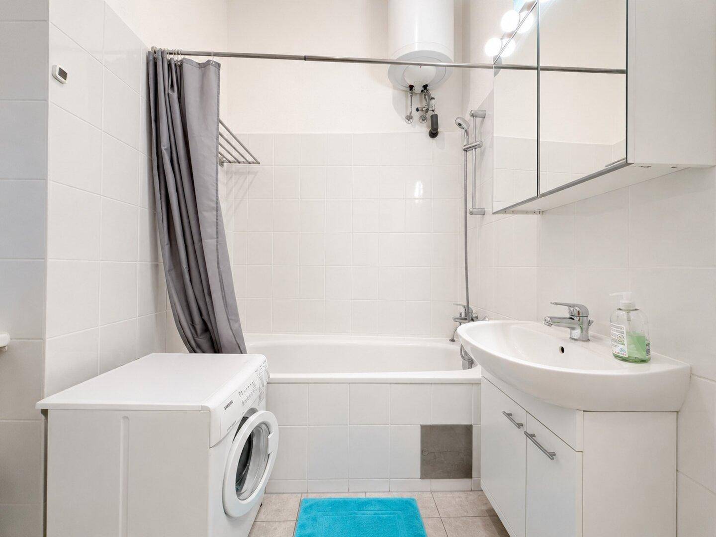 Helles Badezimmer mit Badewanne, Waschmaschine und modernem Waschbecken.