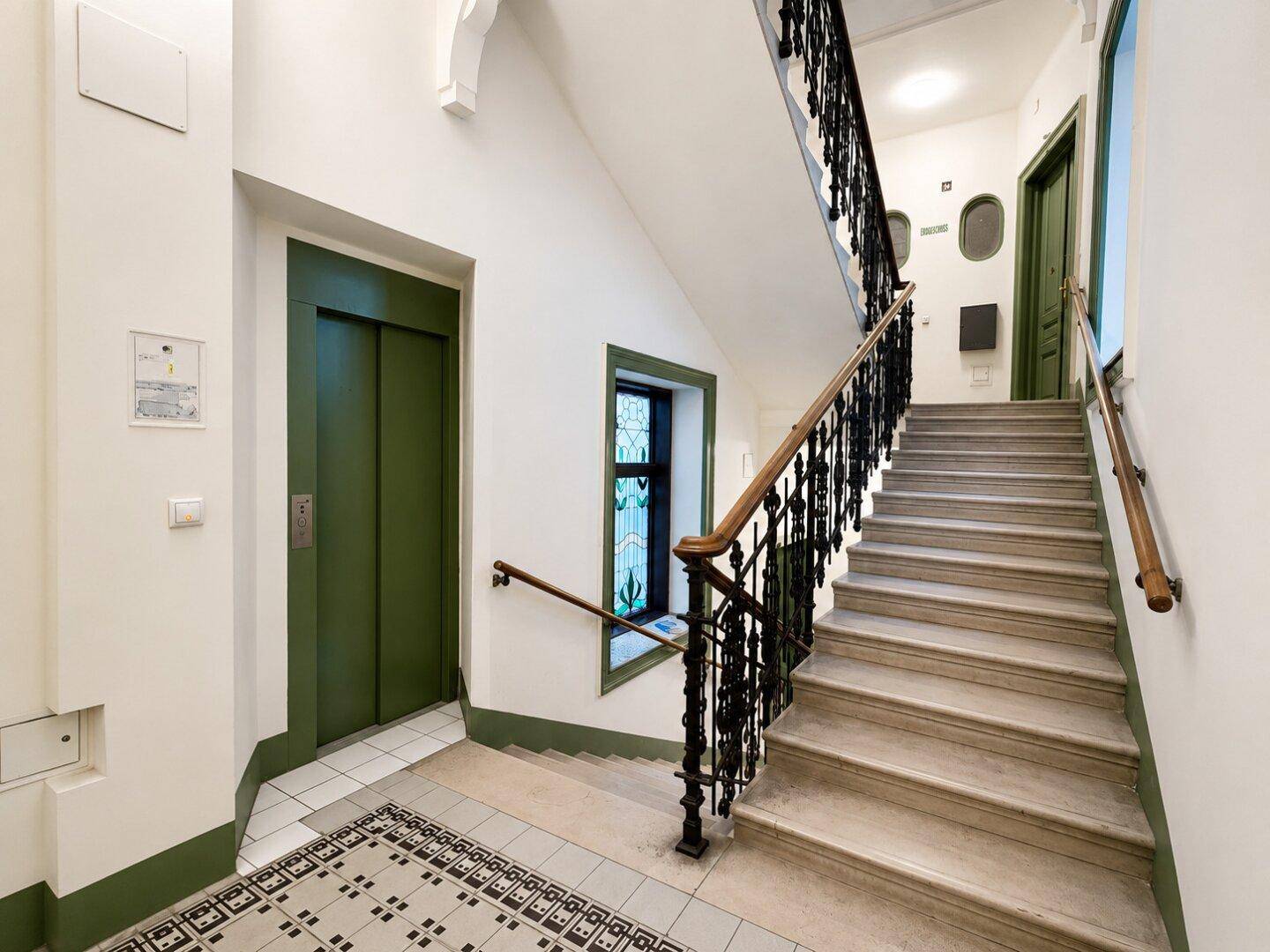 Historisches Treppenhaus mit elegantem Geländer und einem modernen Aufzug.
