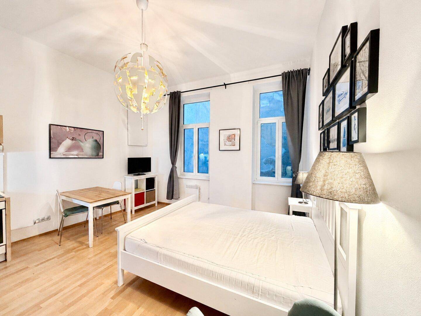 Gemütliches Studio-Apartment mit Bett, Esstisch und moderner Beleuchtung.