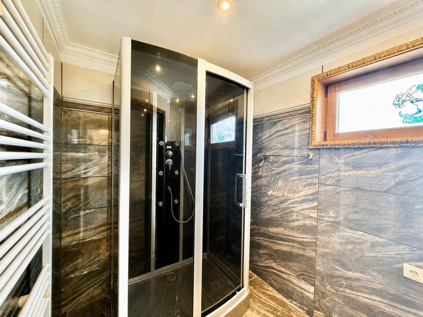 Modernes Badezimmer mit Duschkabine, dunklen Marmorfliesen und beheiztem Handtuchhalter.