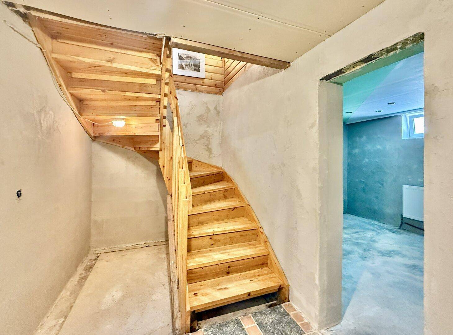 Holztreppe führt in den Kellerbereich mit unverputzten Wänden und einfacher Beleuchtung.