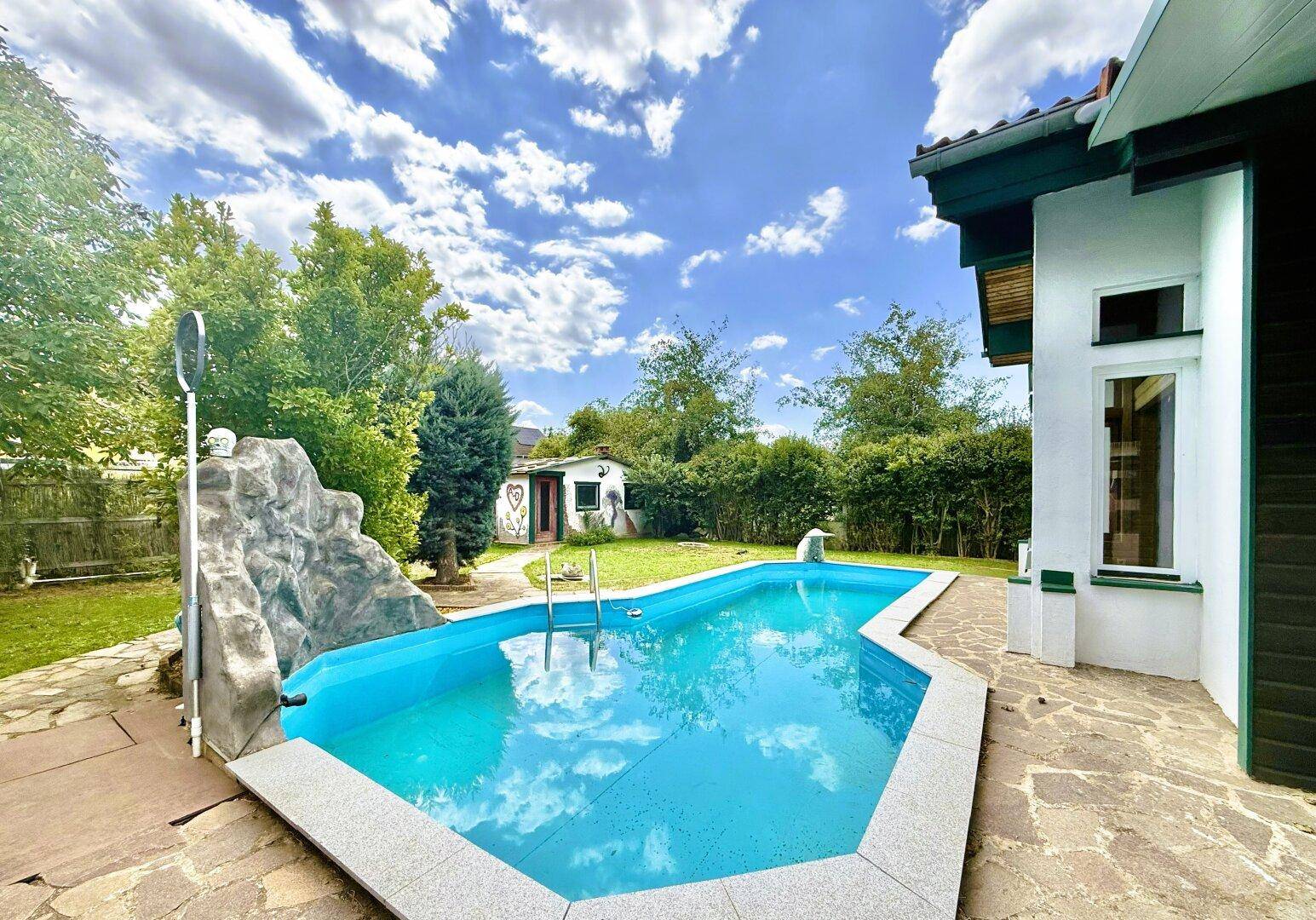 Außenbereich mit privatem Pool, umgeben von einer Steinterrasse und grüner Bepflanzung.