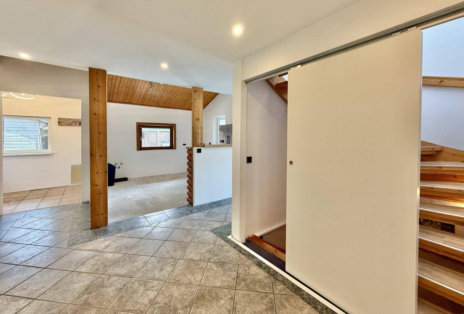 Geräumiger Flur mit Fliesenboden, Holztreppe und sichtbaren Holzstützen.