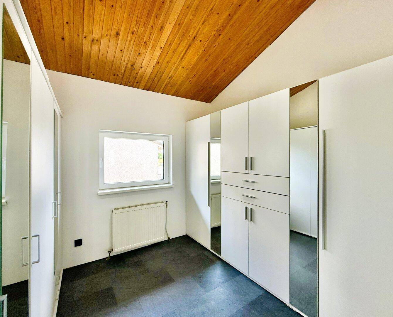 Schlafzimmer mit weißen Einbauschränken, Holzdecke und Fenster für natürliches Licht.