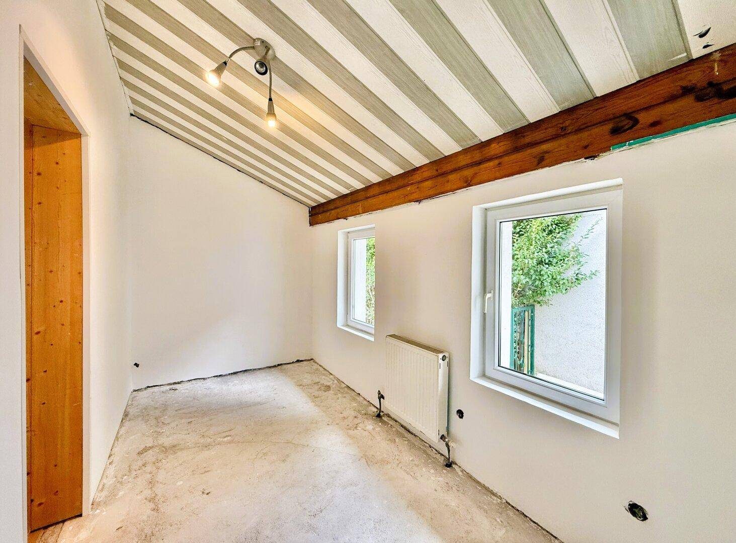 Leerer Raum mit gestreifter Decke, Holzbalken und Fenster, bereit zur Einrichtung.