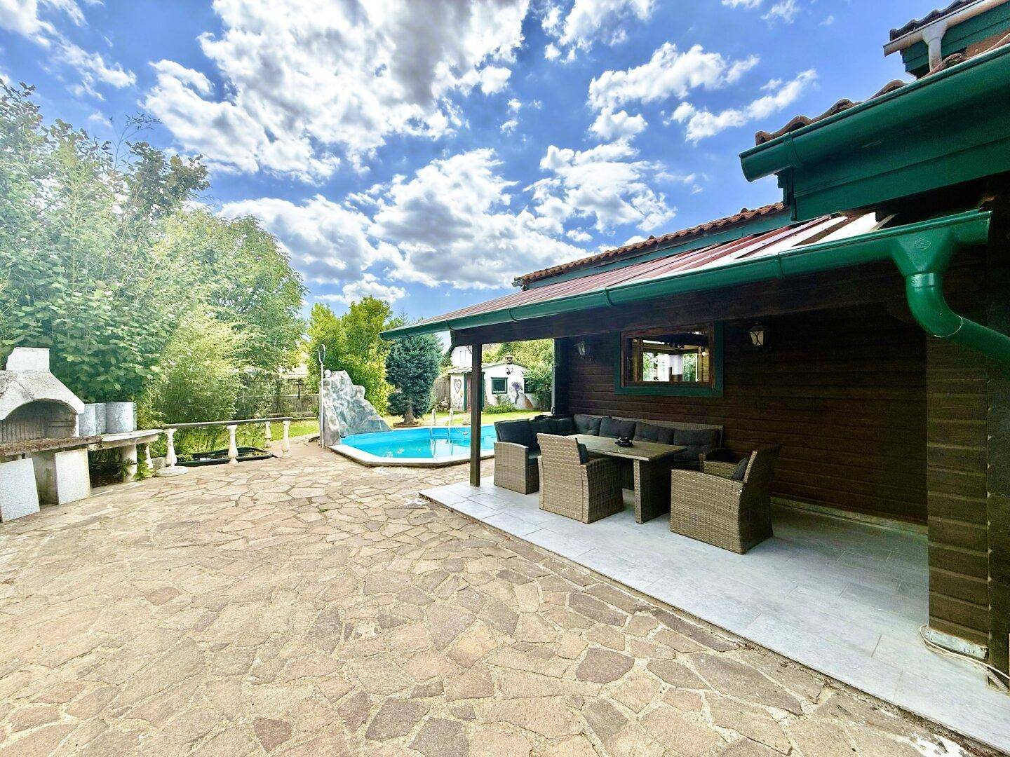 Große Steinterrasse mit überdachtem Essbereich und Grillplatz, Blick auf den Pool.
