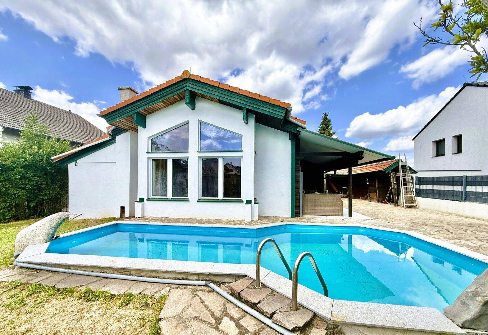 Einfamilienhaus mit privatem Pool im Garten unter blauem Himmel mit Wolken und einer überdachten Terrasse.