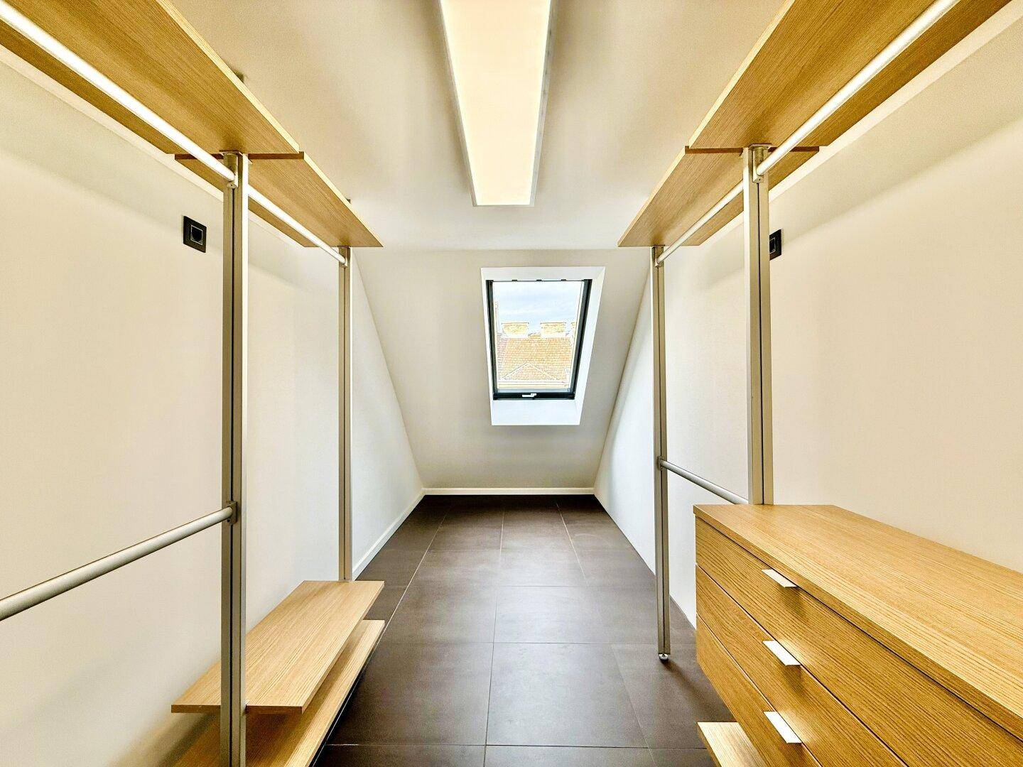 Leerer begehbarer Kleiderschrank mit Regalsystem und Dachfenster, bietet viel Stauraum und Gestaltungsmöglichkeiten.