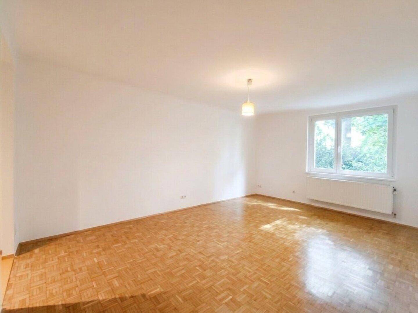 Helles Zimmer mit Parkettboden und einem Fenster, das viel Tageslicht hereinlässt.