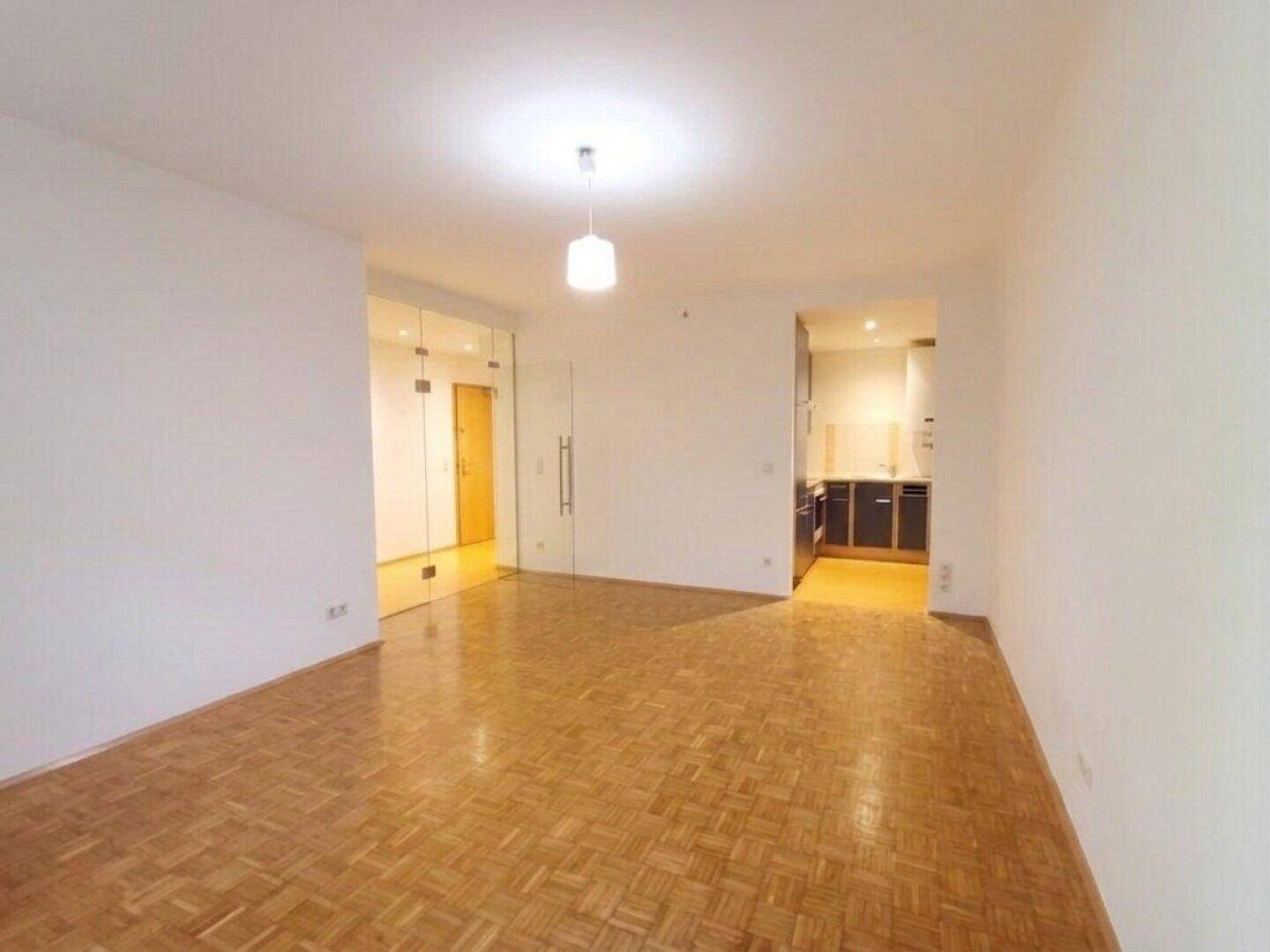 Heller Wohnbereich mit Parkettboden und offenem Zugang zur angrenzenden Küche.