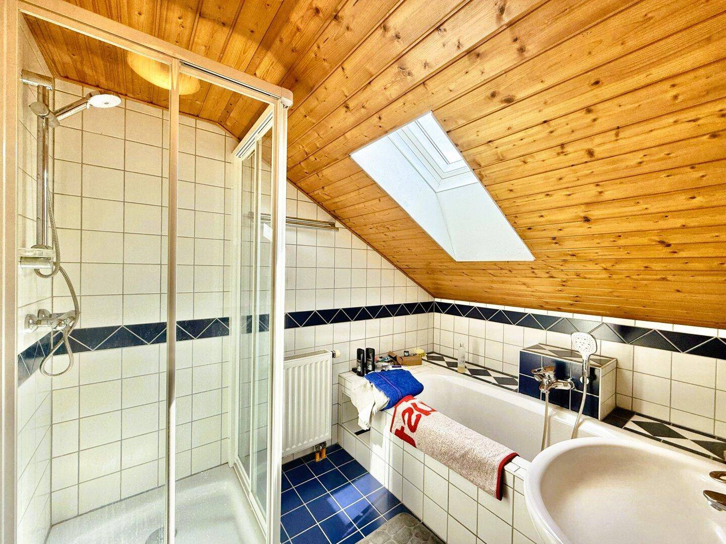 Badezimmer im Dachgeschoss mit Dusche, Badewanne, Waschbecken und Dachfenster.