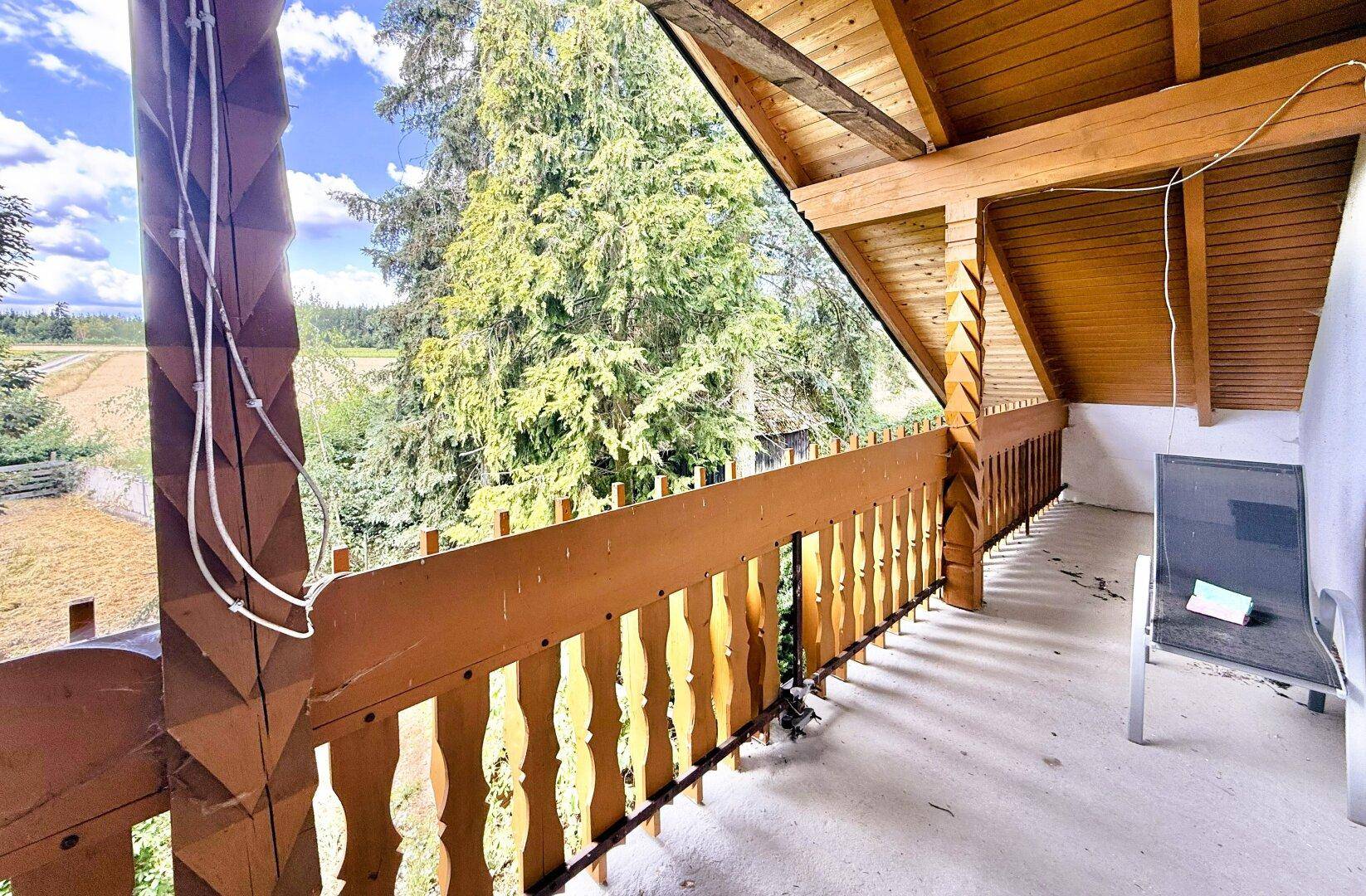 Balkon mit Holzgeländer und weitem Blick über die grüne Landschaft.