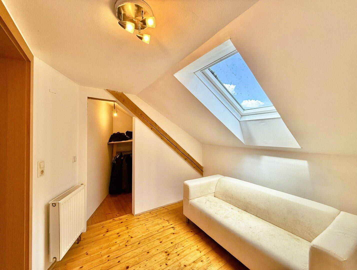 Dachgeschossraum mit Dachfenster, Dielenboden und einem Sofa.