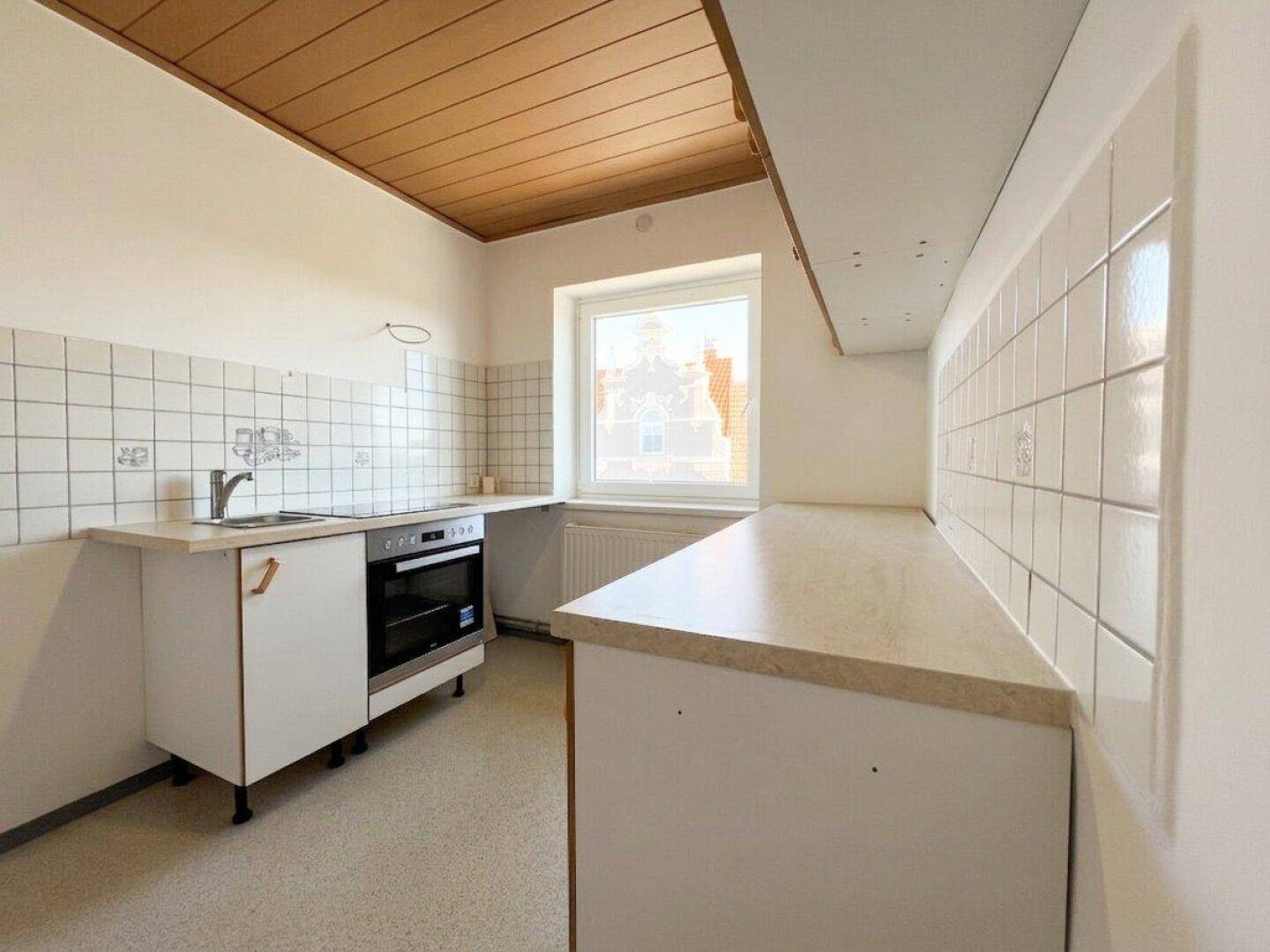 Einfache Küche mit weißen Fliesen, Holzdecke und Fensterblick nach draußen.