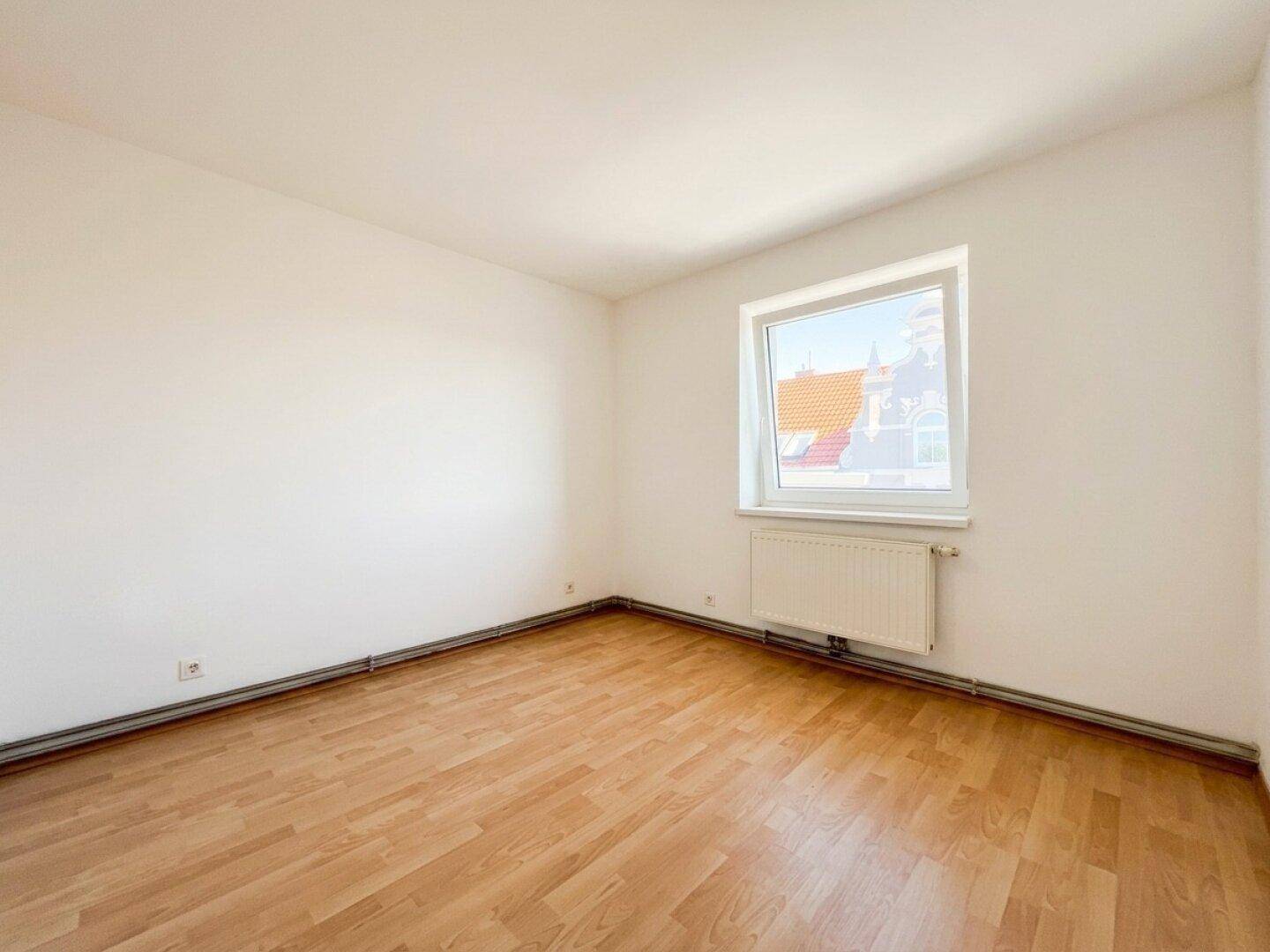 Helles Zimmer mit Laminatboden, weiß gestrichenen Wänden und einem Fenster.