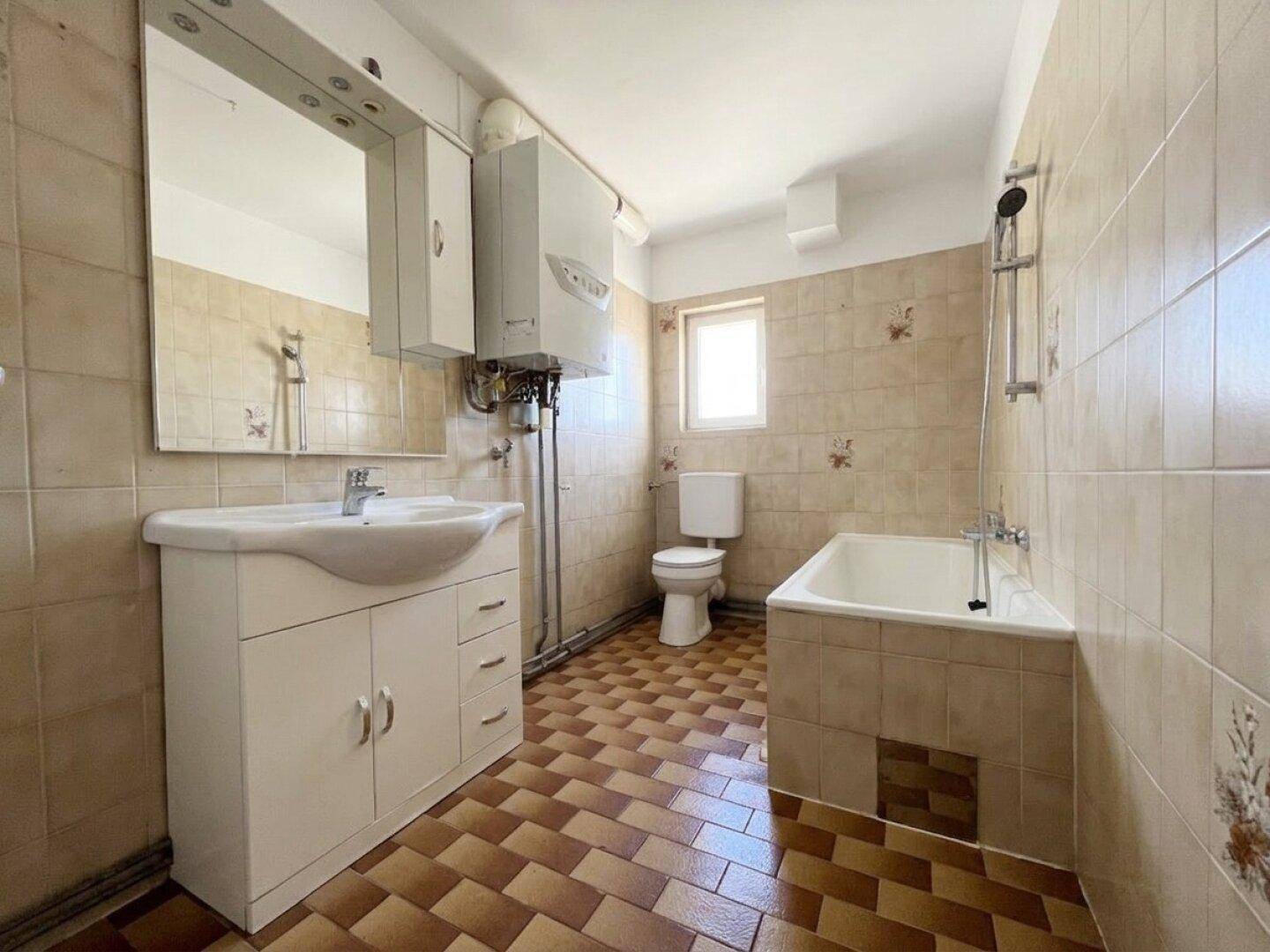 Badezimmer mit beigen Fliesen, Badewanne, Waschbecken und Fenster.