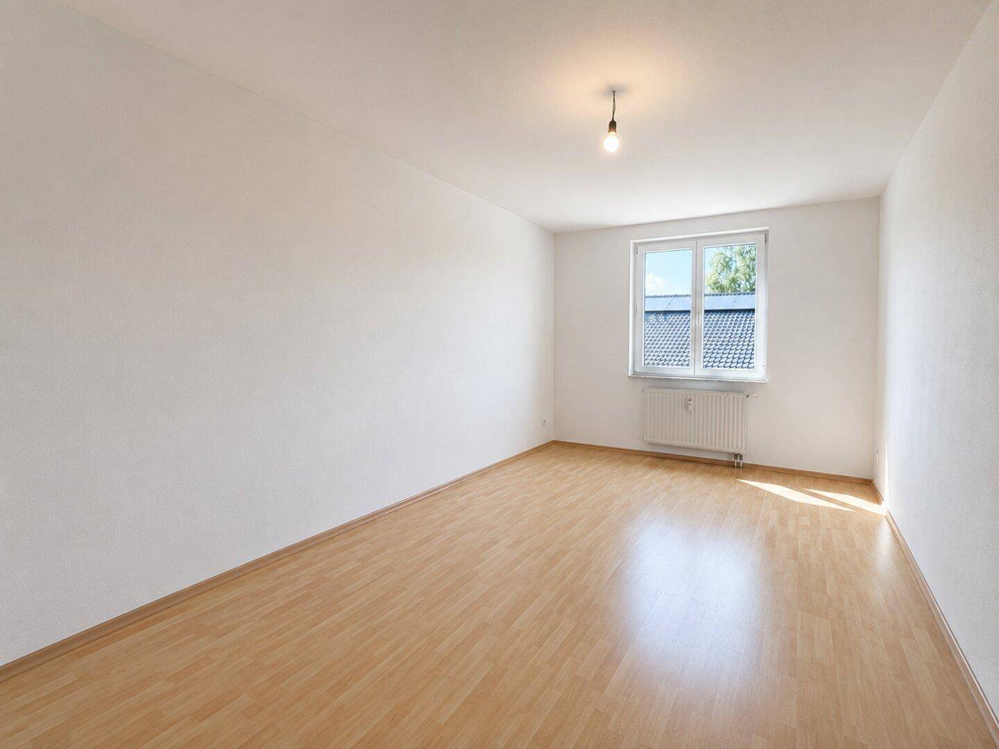 Helles Schlafzimmer mit Holzboden und einem Fenster, das viel natürliches Licht hereinlässt.