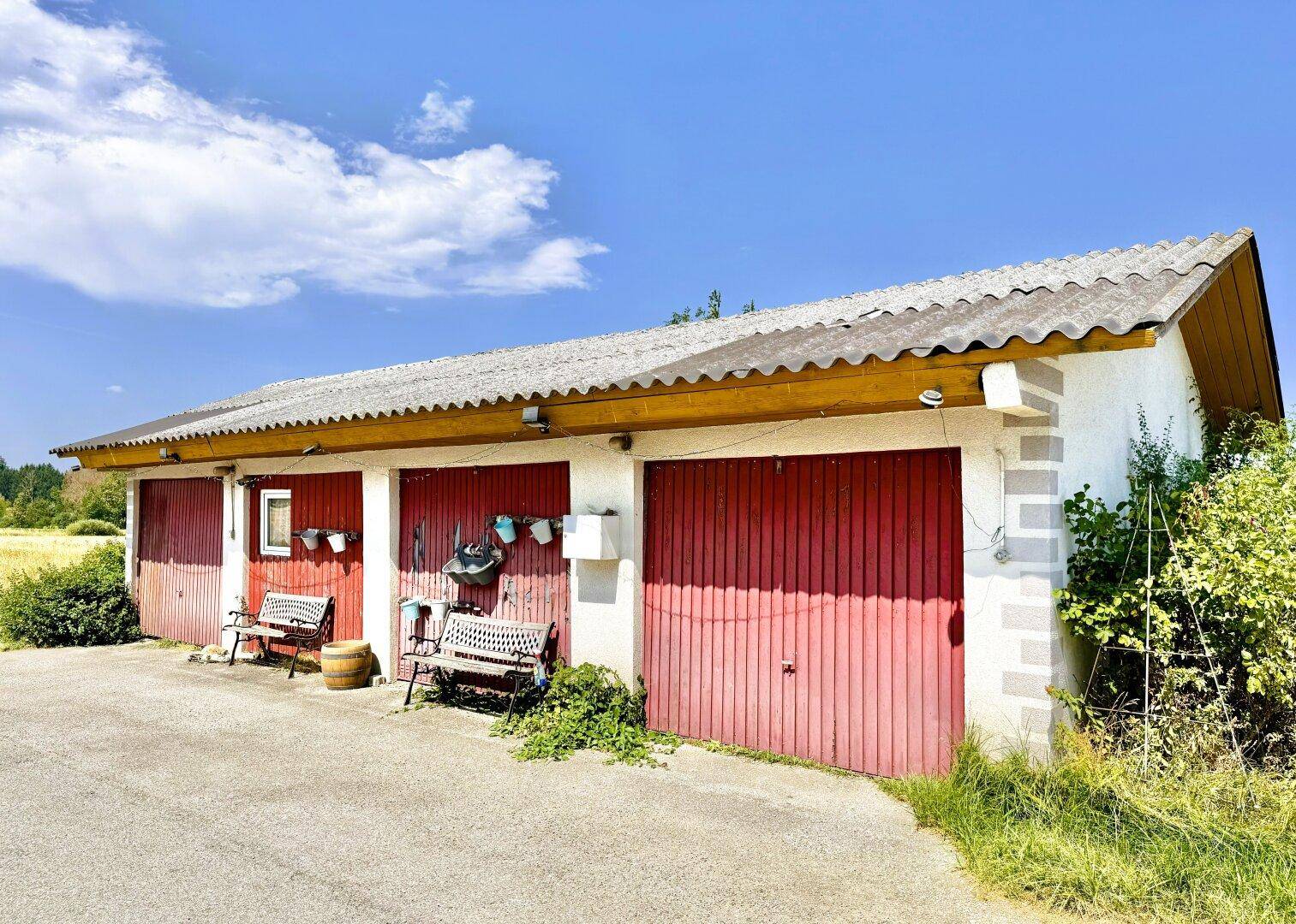 Separate Garage mit drei roten Toren und Stellplätzen davor.