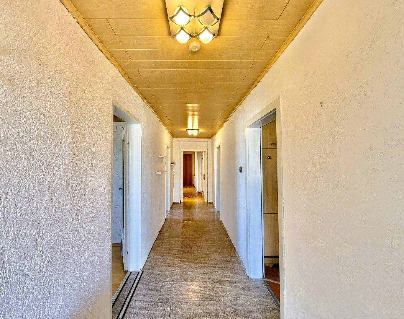 Langer Flur mit Holzdeckenverkleidung und hellen Fliesenboden.