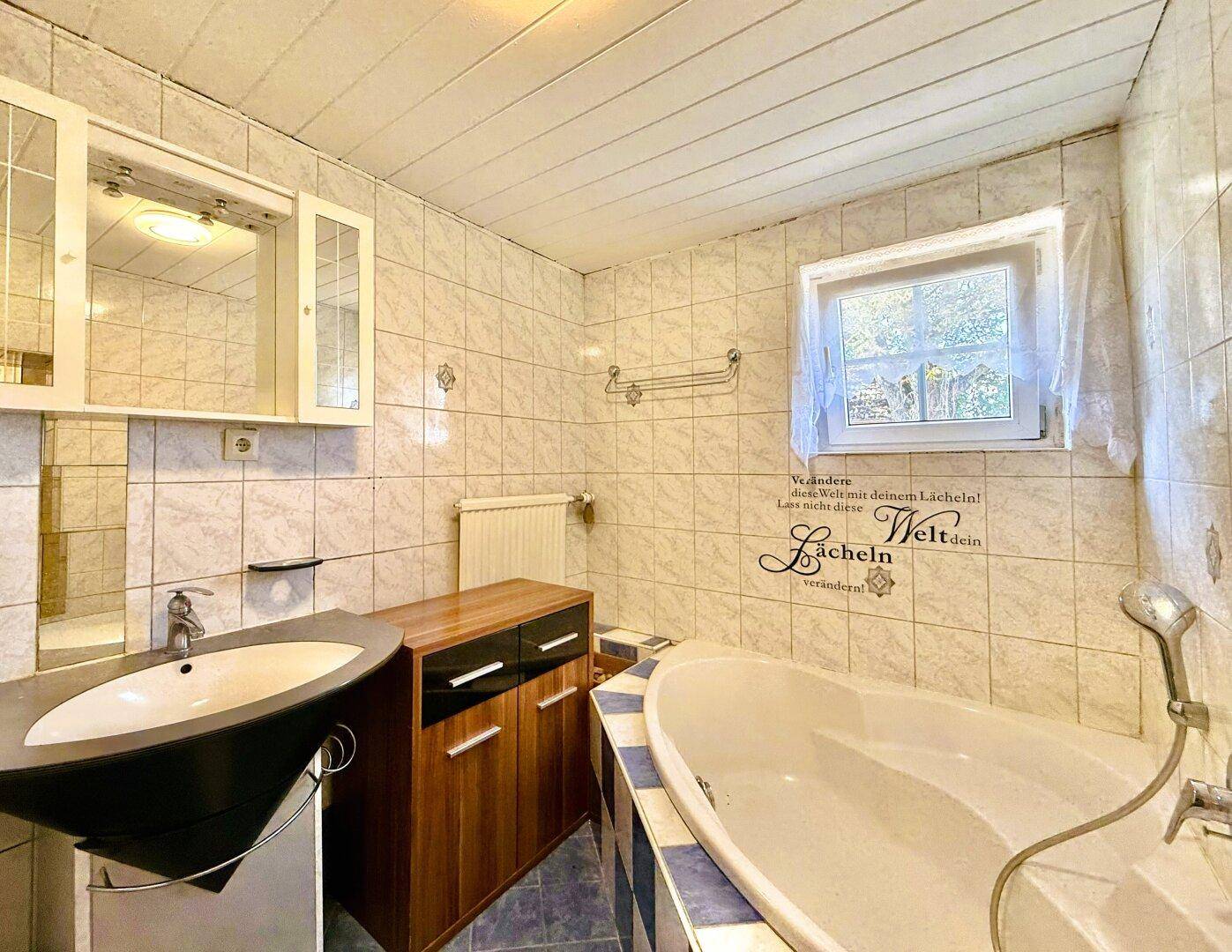 Badezimmer mit Badewanne, Waschbecken und hellen Fliesen an Wänden und Boden.