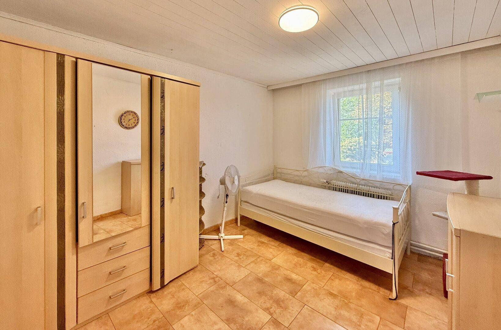 Schlafzimmer mit Einzelbett, Kleiderschrank und Fliesenboden.