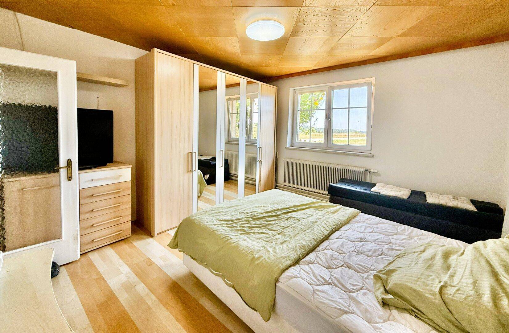 Schlafzimmer mit Doppelbett, Spiegelschrank und Holzfußboden.