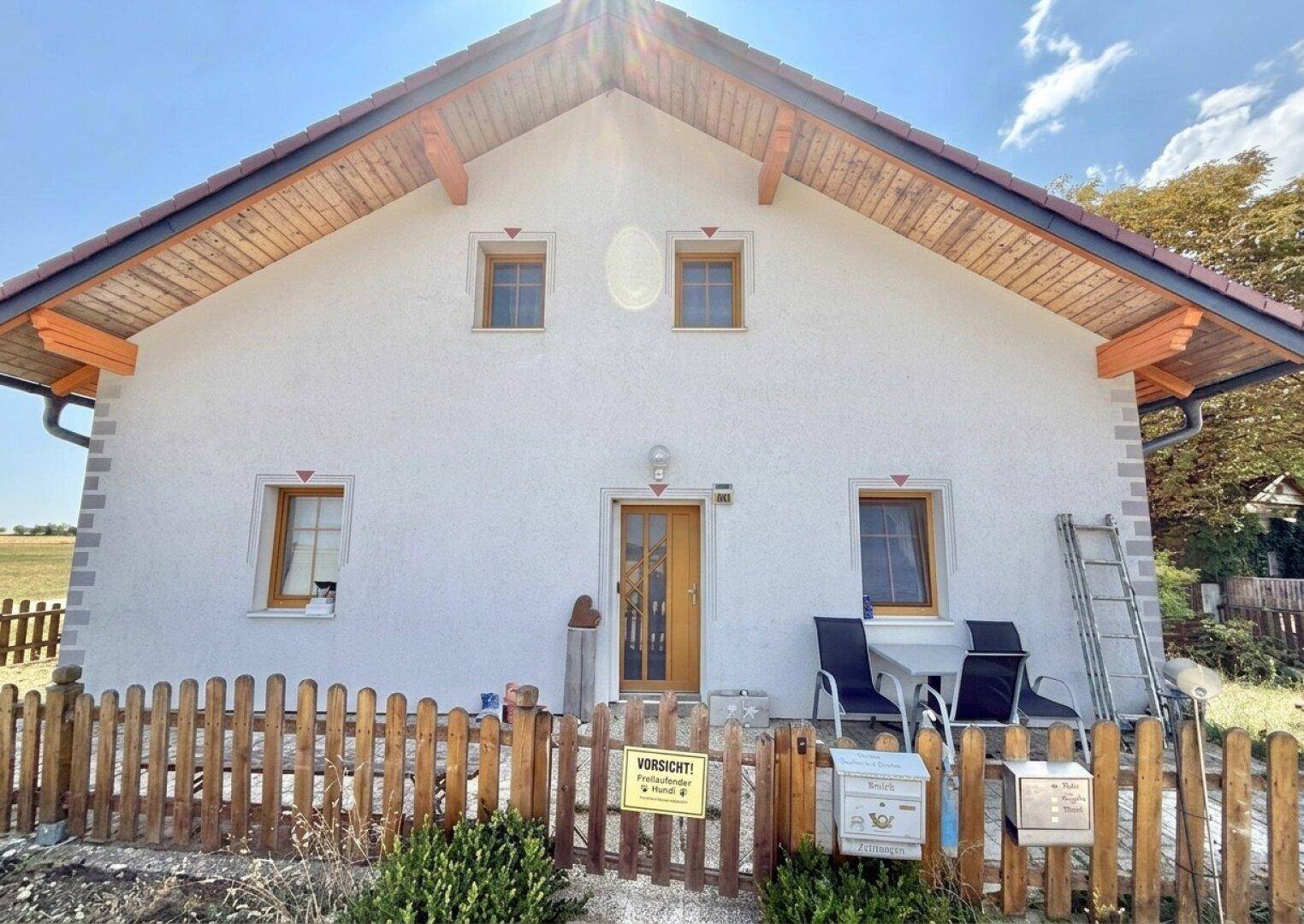 Vorderansicht des Hauses mit weißer Fassade, Holztür und kleinen Fenstern.