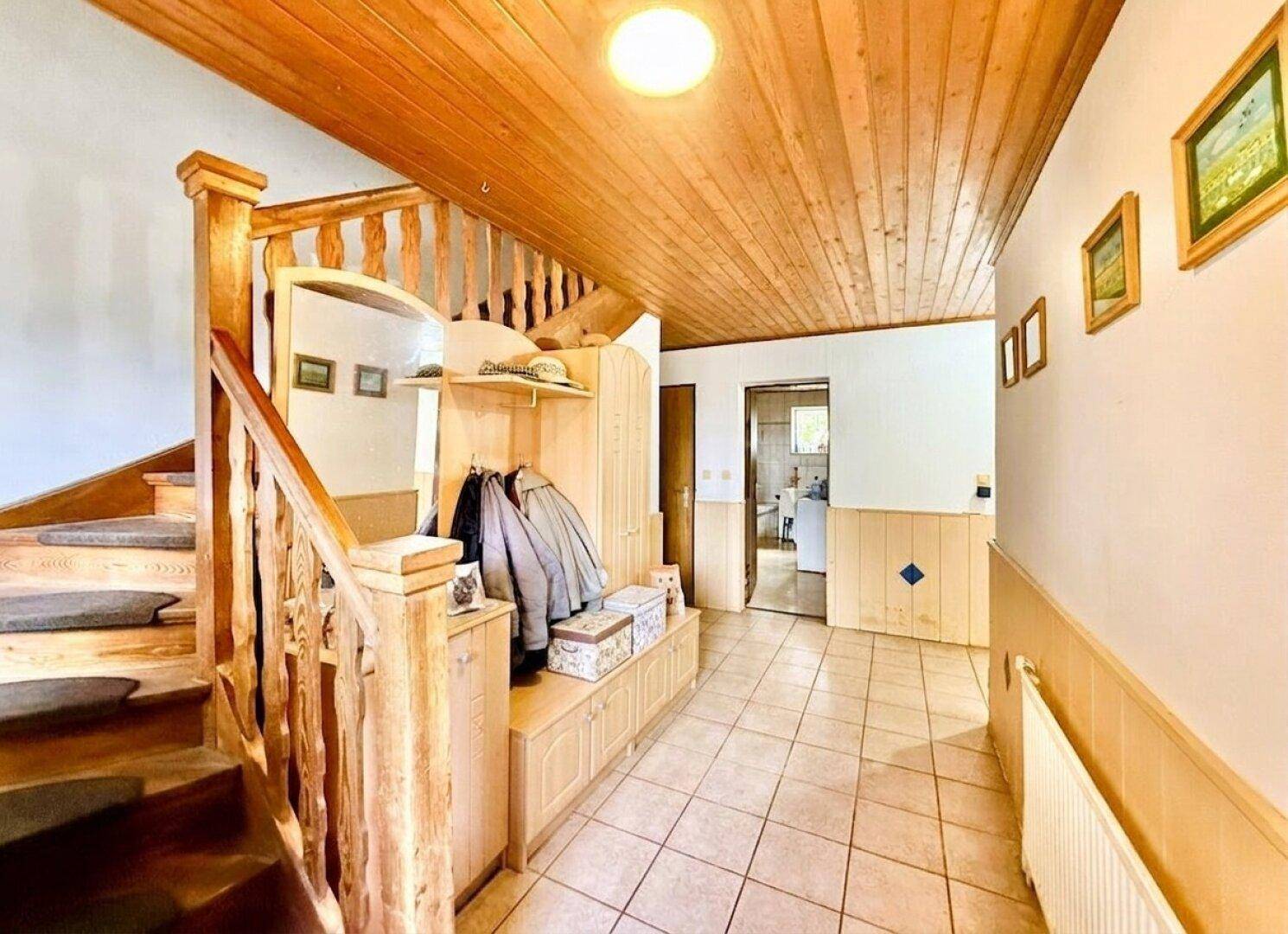 Eingangsbereich mit Holztreppe, Fliesenboden und Holzdeckenverkleidung.