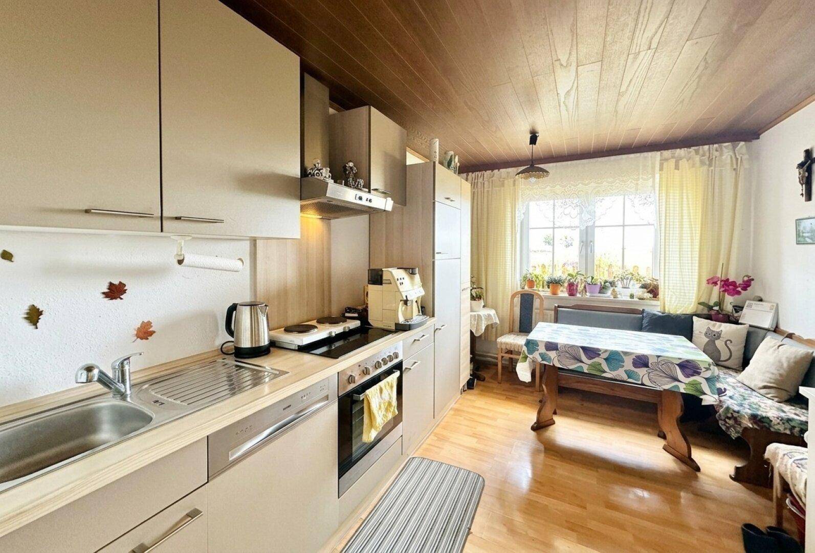 Küche mit hellgrauen Einbauschränken, Essbereich und Holzdeckenverkleidung.