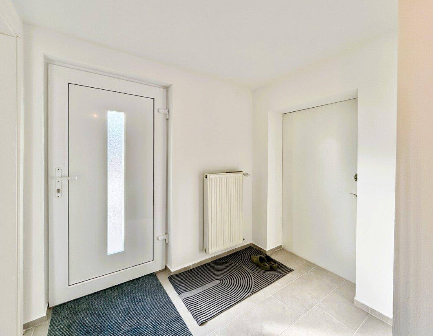 Heller Eingangsbereich mit weißer Haustür, Fliesenboden und Heizkörper.