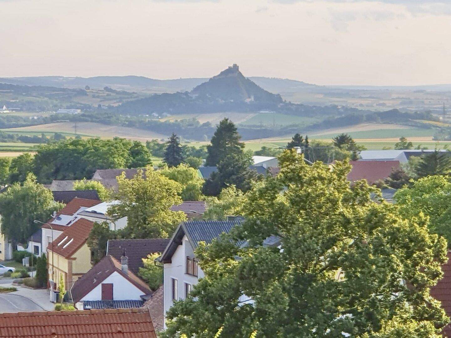 Weitläufiger Blick über eine ländliche Gegend mit einem Dorf und einer Burg auf einem Hügel.