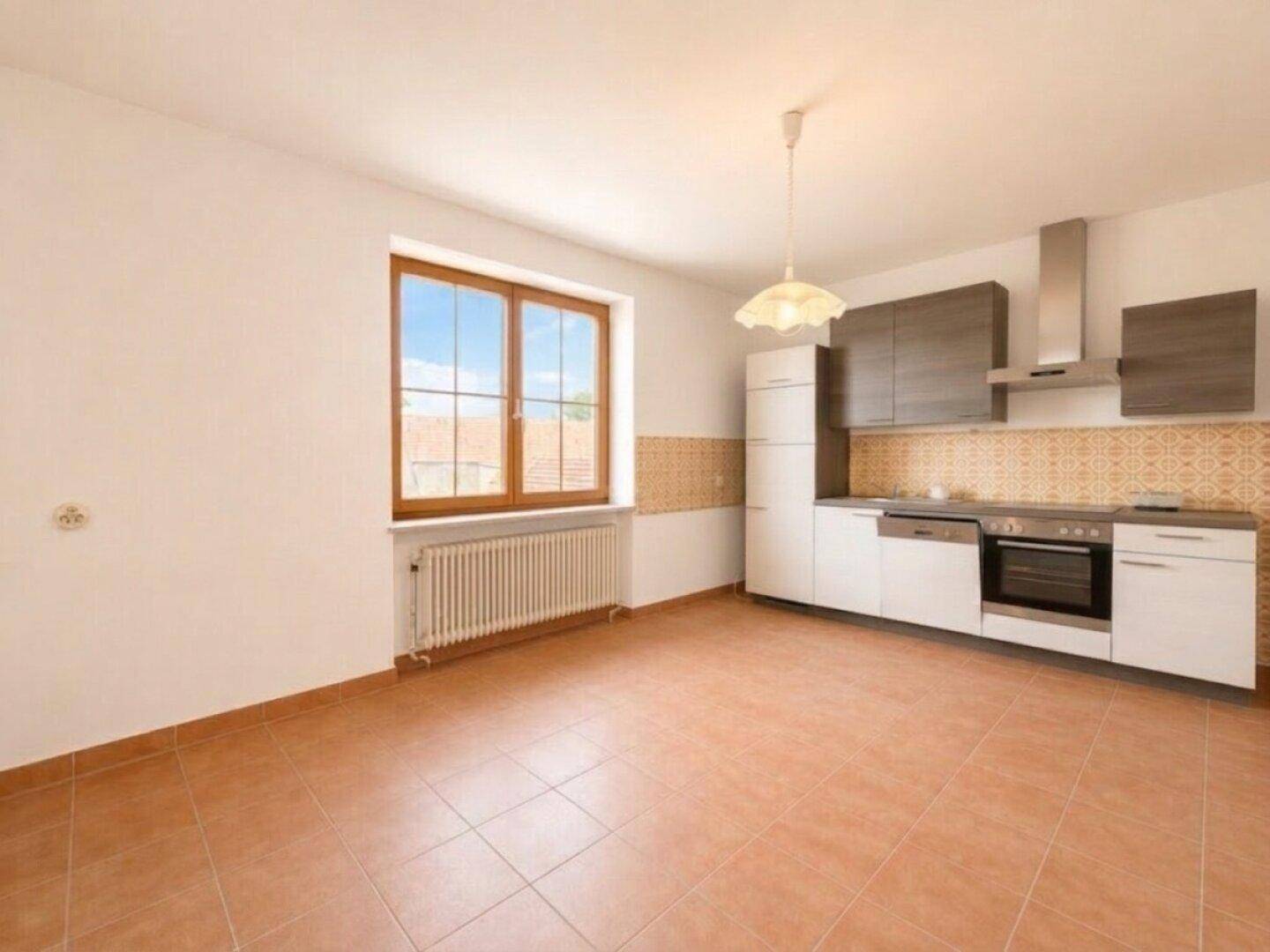 Küche mit weißen und grauen Schränken, modernen Geräten und Terrakotta-Fliesenboden.