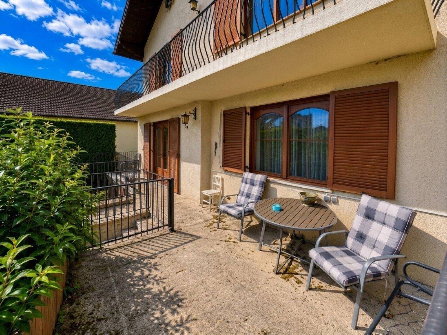 Außenterrasse mit Sitzgelegenheiten, umgeben von Grünpflanzen und Blick auf das Haus.