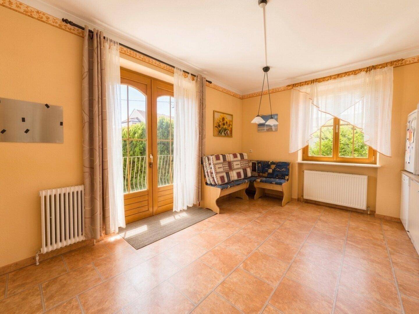 Essbereich mit Terrakotta-Fliesenboden, eingebauter Sitzbank und Zugang zu einem französischen Balkon.