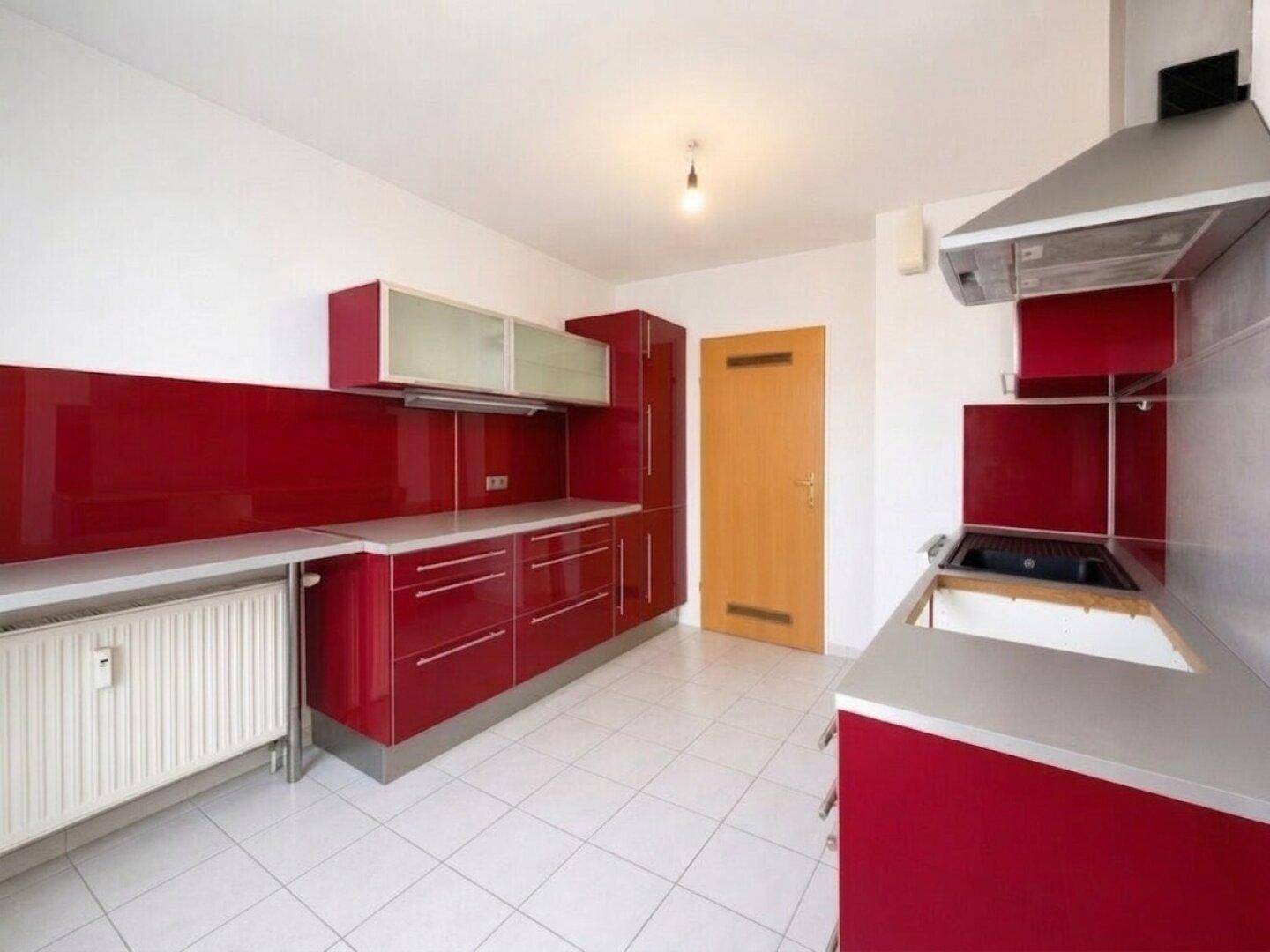 Moderne Einbauküche mit leuchtend roten Hochglanzfronten, weißen Fliesen und Dunstabzugshaube.