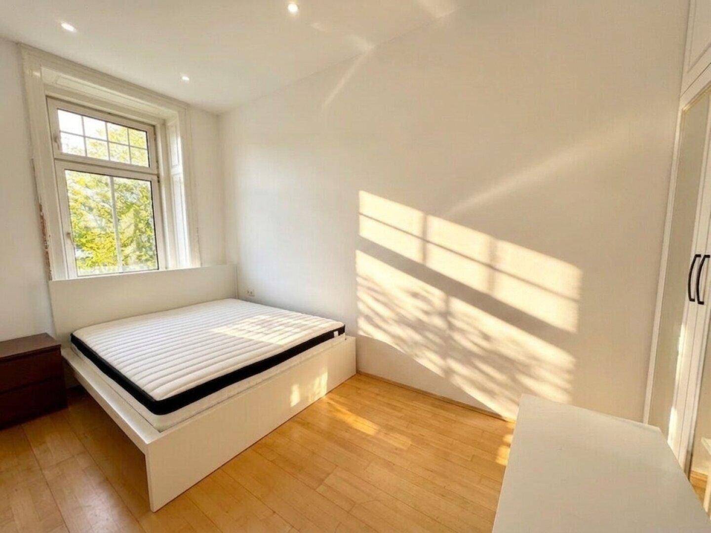 Schlafzimmer mit Doppelbett, Holzboden und viel natürlichem Licht durch das große Fenster.